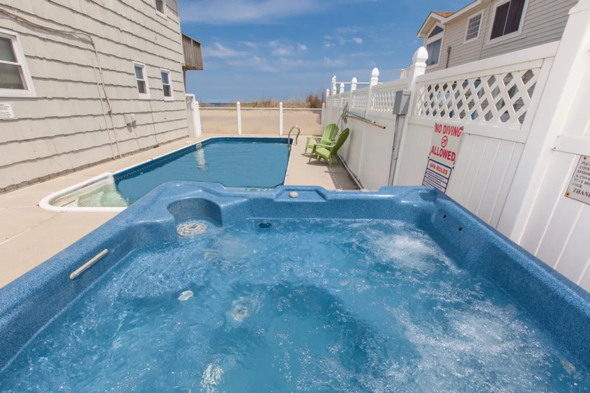 This image presents a private backyard area featuring a swimming pool and a hot tub, bordered by a fence for privacy. A lounge chair sits nearby, inviting relaxation, while the overall setting suggests a space ideal for both family gatherings and quiet moments. The presence of the fence emphasizes the sense of exclusivity and safety.