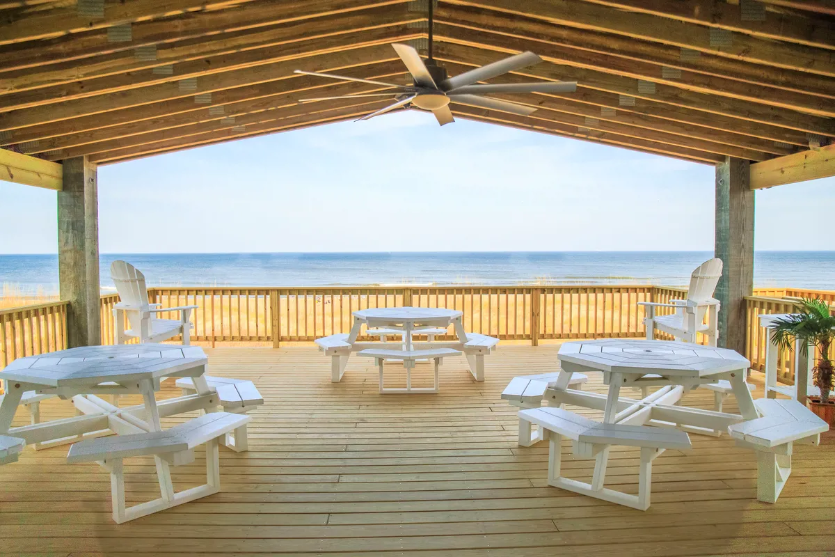 An inviting outdoor space featuring several picnic tables and classic Adirondack chairs, all facing a stunning ocean view. The area is designed for group meals, relaxation, and socializing, with a peaceful, welcoming ambiance that encourages families to spend time outside together.