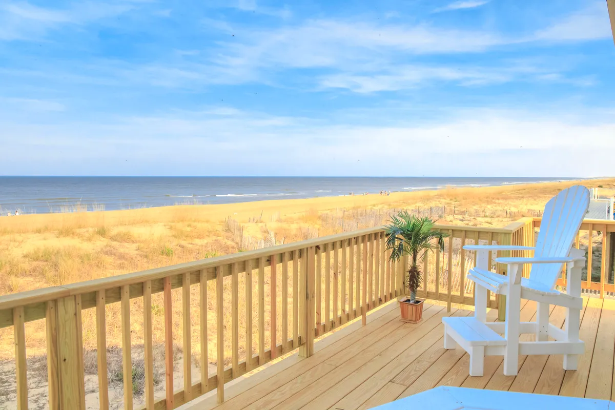 A serene exterior scene featuring a wooden deck overlooking the ocean, with a single chair and a potted plant as focal points. The backdrop includes calming water views and open sky, evoking a sense of tranquility and relaxation.