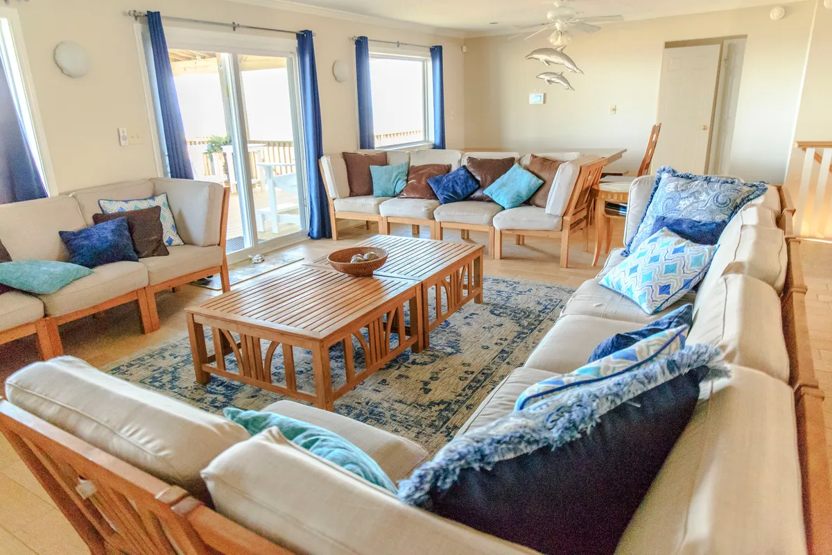 This image shows a comfortable and welcoming living room with a sofa set, decorative pillows, coffee table, area rug, and large sliding glass doors that let in ample natural light. The arrangement suggests a space designed for gathering, socializing, and relaxing, with an inviting ambiance fit for both intimate family moments and larger festive occasions.